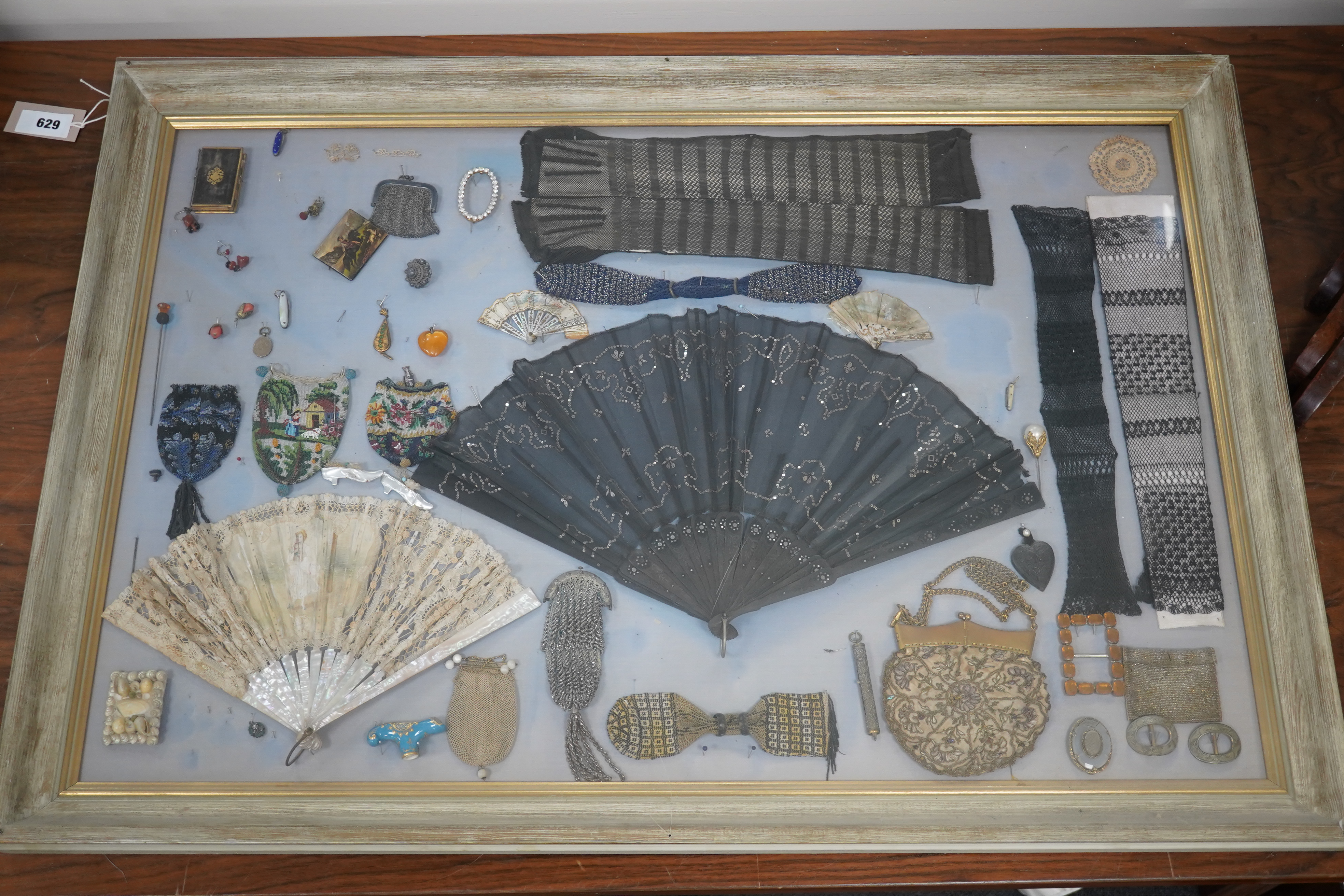 A framed display montage of late 18th and 19th century decorative ladies sequin and lace fans, beadwork reticules, cut steel misers purses, hat pins, earrings, brooches, shoe buckles and crochet mittens.100cm x 70cm. Con